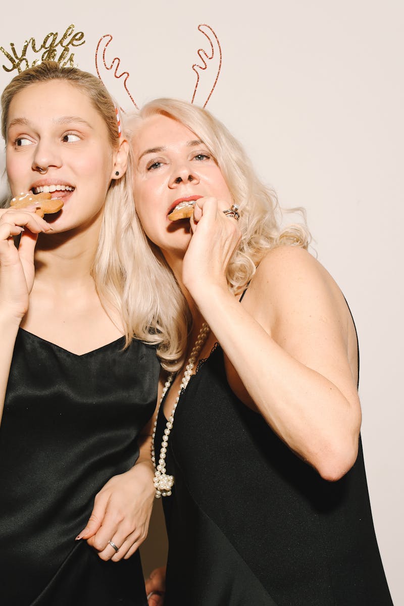 Two women enjoying holiday cookies, wearing festive attire with holiday headbands.
